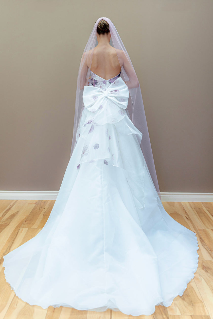 Back view of the floral couture gown, featuring a dramatic large bow at the waist that complements the A-line skirt and cathedral veil.