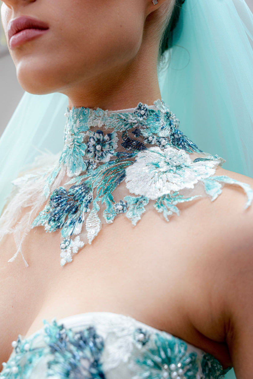 Close-up of aqua wedding gown illusion high-neck bodice with intricate floral embroidery and beadwork.