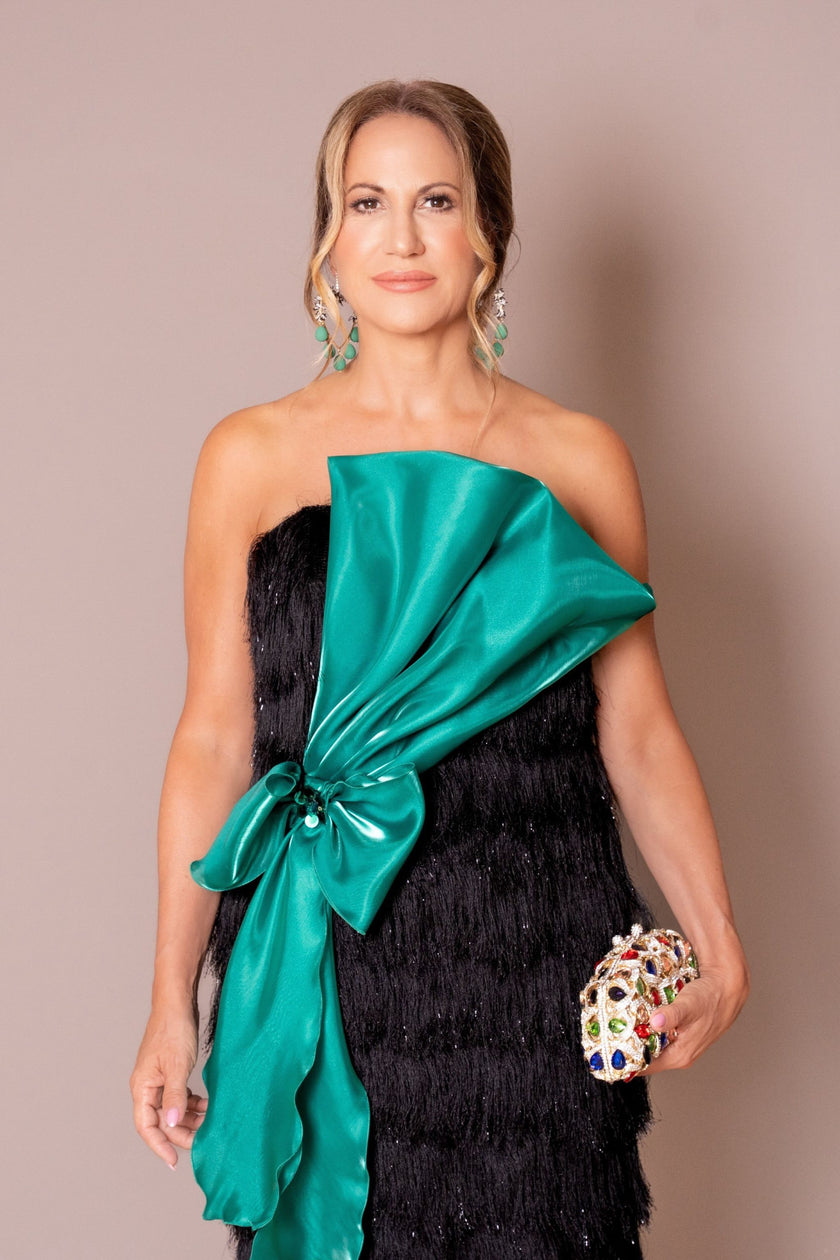 Black fringe gown with sheer long sleeves and a dramatic emerald satin bow.