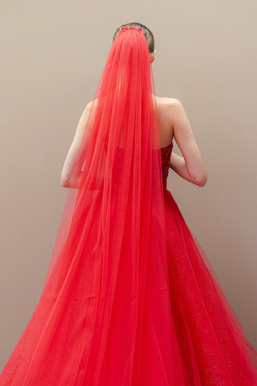 Back view of the red couture ball gown, showcasing the dramatic sweep of the long cathedral veil against the voluminous tulle skirt.