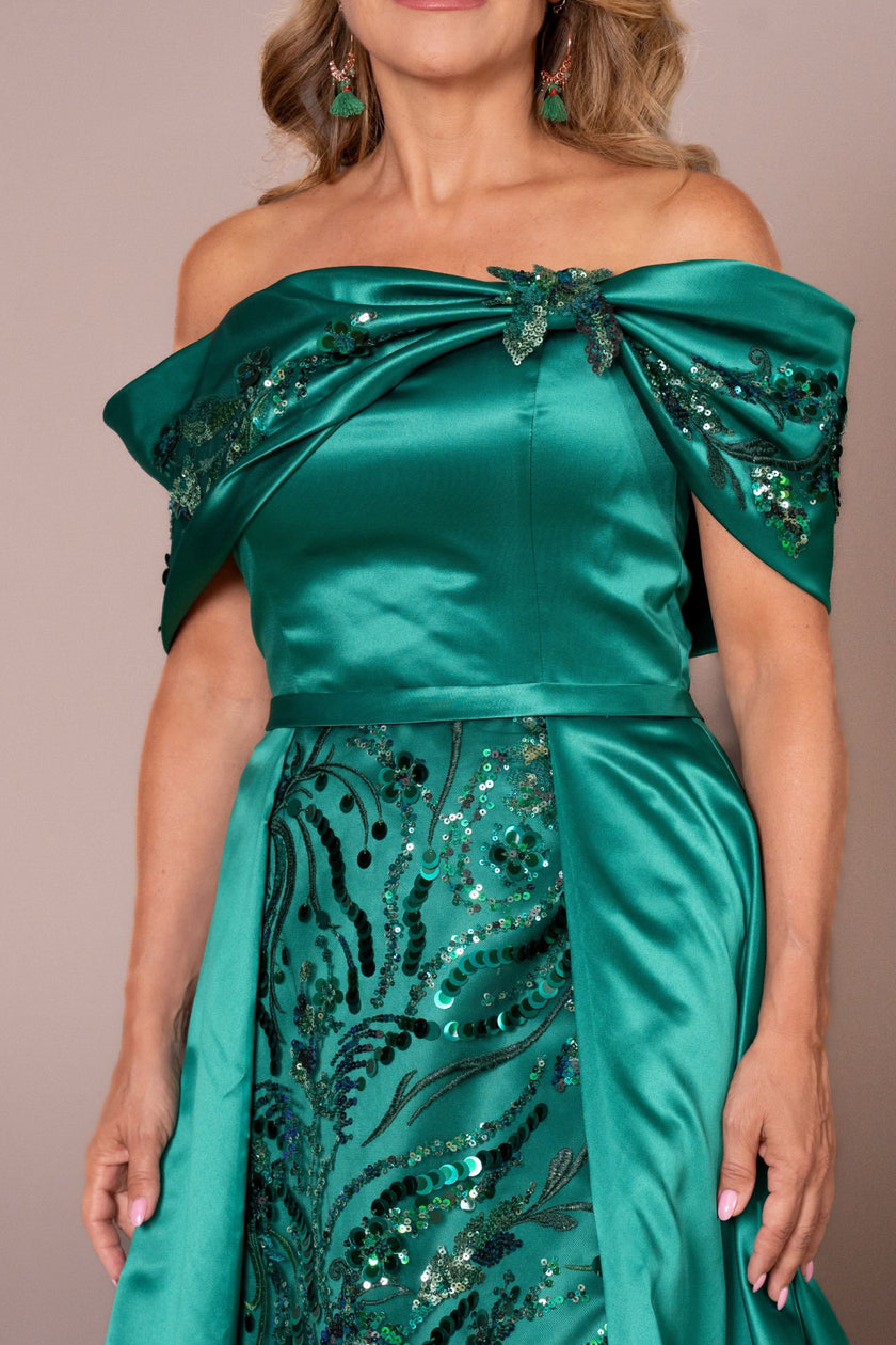 Woman in an emerald green couture gown with a structured overskirt and off-the-shoulder neckline.