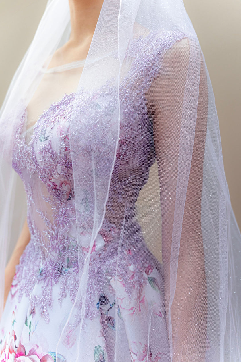 Close-up of a floral couture wedding gown with a sheer overlay and a veil.