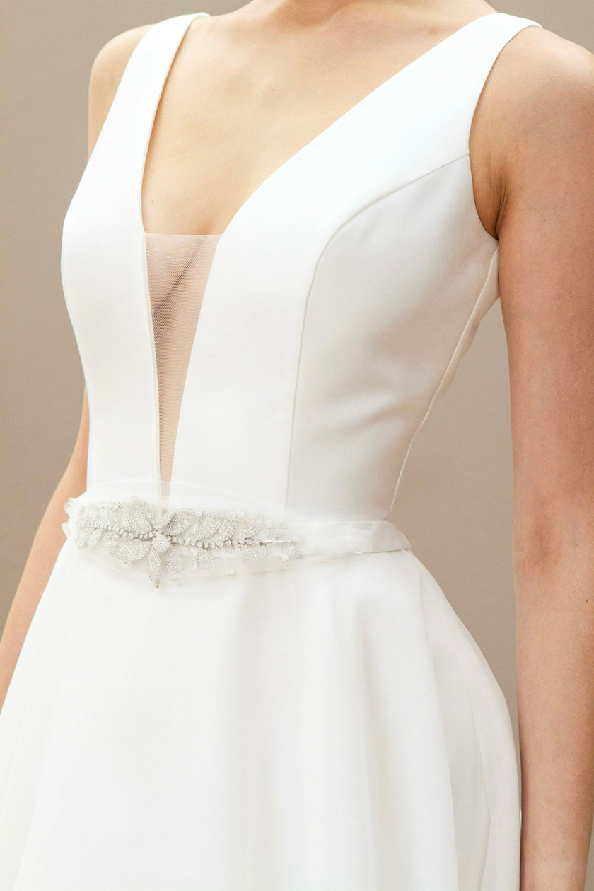 Close-up of the deep V-neckline and hand-beaded waistband on a sleeveless modern wedding gown.