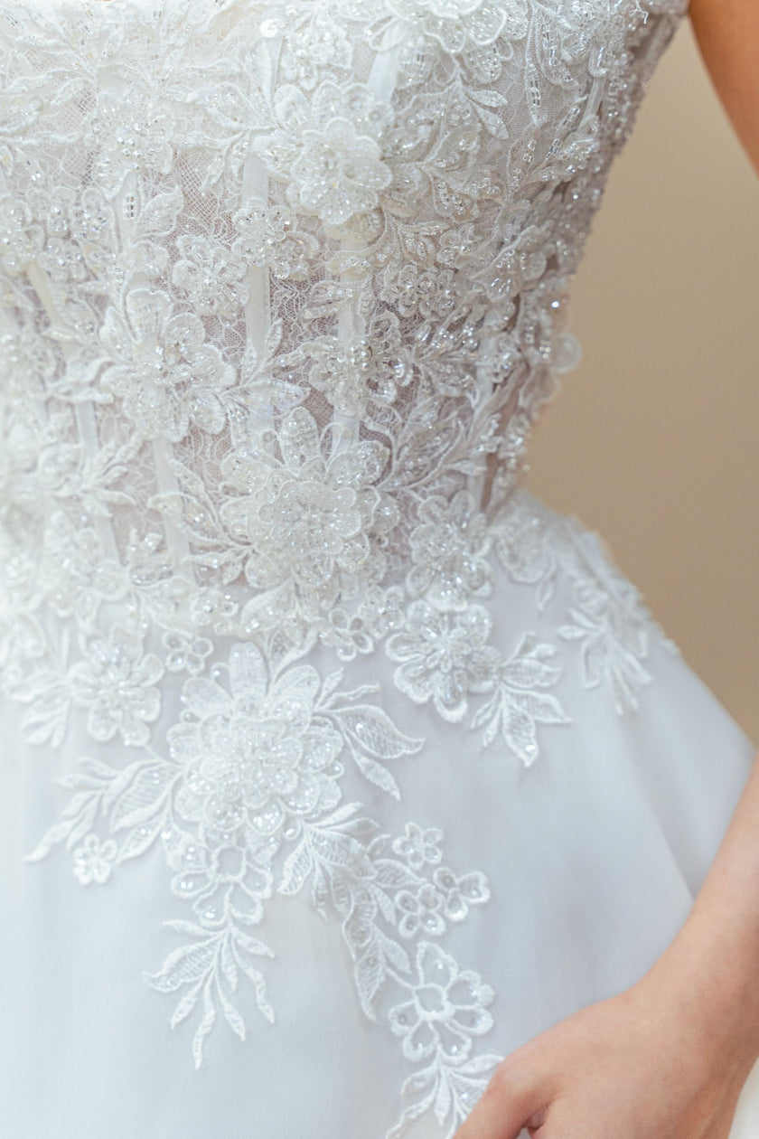 Close-up of strapless lace wedding dress bodice with intricate floral embroidery and Swarovski crystals.