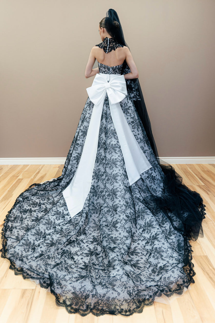 Black and white couture wedding gown with a large white bow, showcased on a wooden floor against a neutral beige wall.