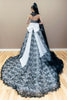 Black and white couture wedding gown with a large white bow, showcased on a wooden floor against a neutral beige wall.