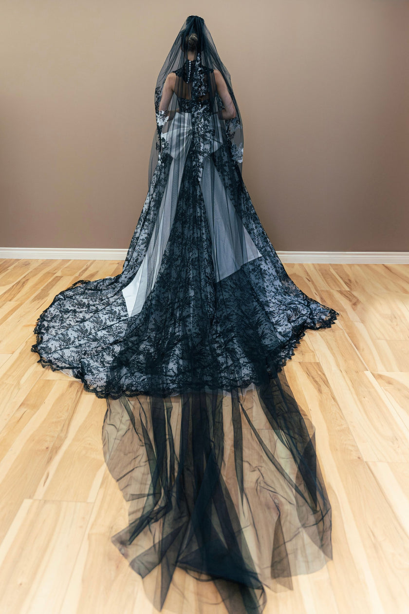 Black lace wedding dress with a long train, featuring a dramatic oversized white bow.