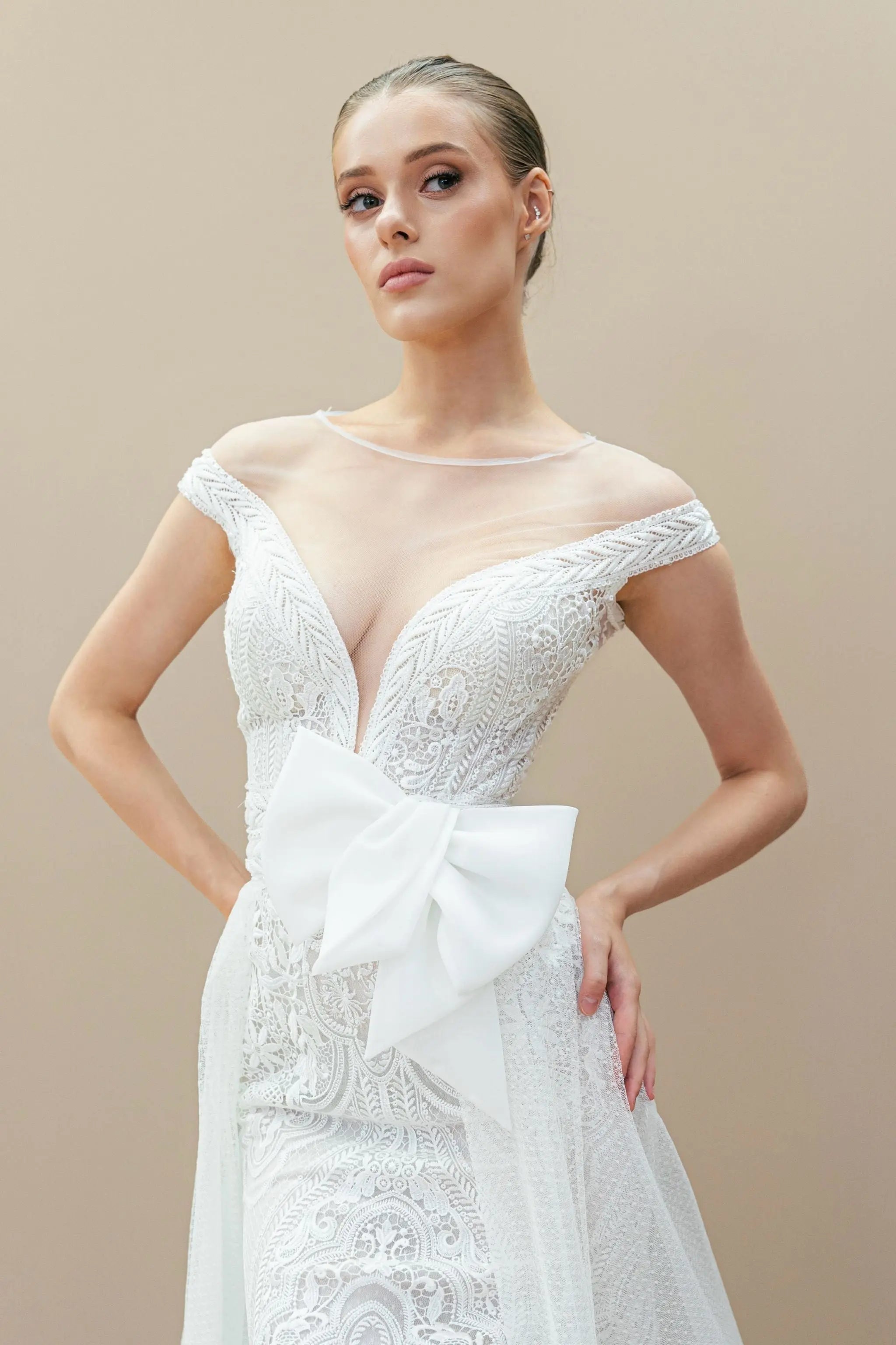 Front view of lace mermaid wedding gown with illusion neckline and oversized bow.